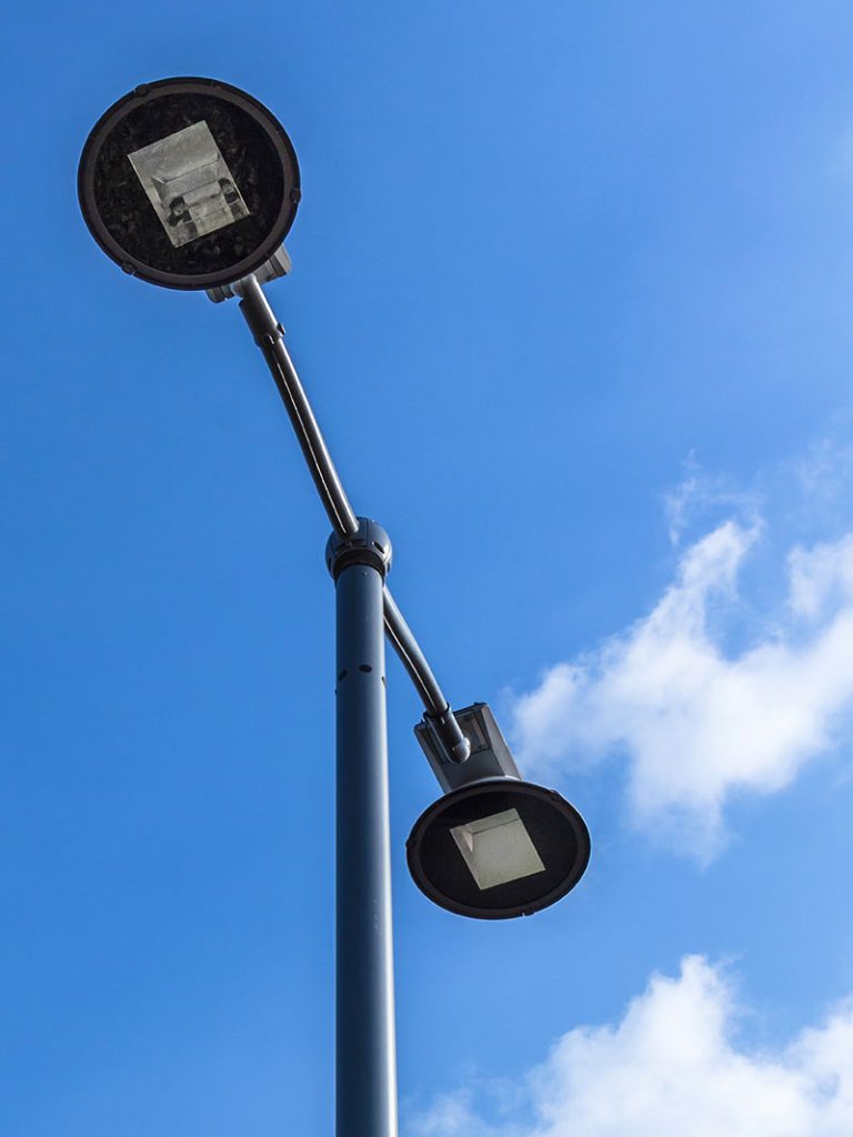 A close-up view of a dual-head LED street light with a bright blue sky and a few clouds in the background.