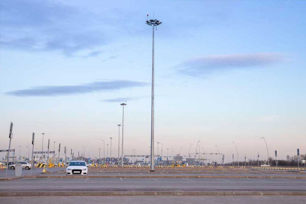 A spacious parking lot with a single white car, tall light poles, and a clear evening sky in the background, featuring soft clouds and a serene urban environment.